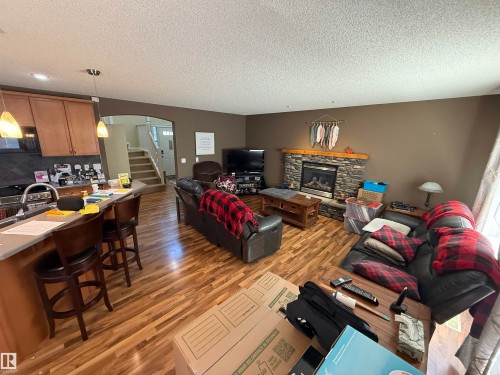 Open concept living space featuring a kitchen with light wood cabinetry, a breakfast bar, and pendant lighting, and a living area with a stone-faced fireplace, and hardwood-style flooring throughout - 21113 92A Avenue, Edmonton, AB - Indoor With Fireplace