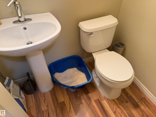 Bathroom featuring a white pedestal sink with a chrome faucet, a white toilet, and wood-patterned flooring - 21113 92A Avenue, Edmonton, AB - Indoor Photo Showing Bathroom