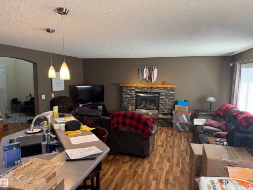 This inviting living area features warm-toned walls, durable wood-look flooring, and a stone-faced fireplace with a wooden mantel - 21113 92A Avenue, Edmonton, AB - Indoor Photo Showing Living Room With Fireplace
