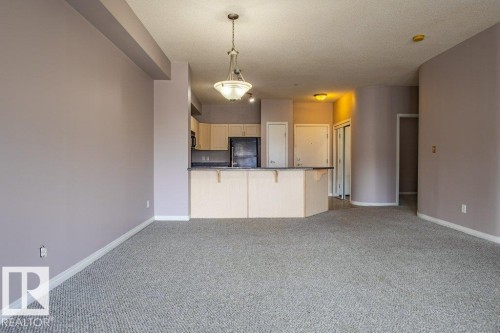 Open-concept living area featuring light gray carpeting, neutral-toned walls, a kitchen island with a dark countertop, and a chandelier light fixture - 326 4304 139 Ave, Edmonton, AB - Indoor Photo Showing Kitchen