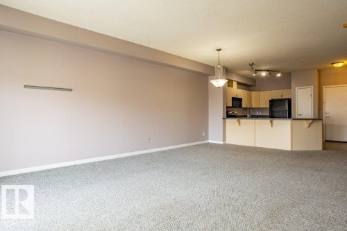 Open concept living space featuring neutral-toned carpeting, a chandelier, and a kitchen area with light-colored cabinetry, dark countertops, and black appliances - 326 4304 139 Ave, Edmonton, AB - Indoor Photo Showing Kitchen
