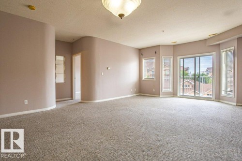 Spacious living area featuring neutral carpeting, light-colored walls, and large windows with blinds - 326 4304 139 Ave, Edmonton, AB - Indoor Photo Showing Other Room