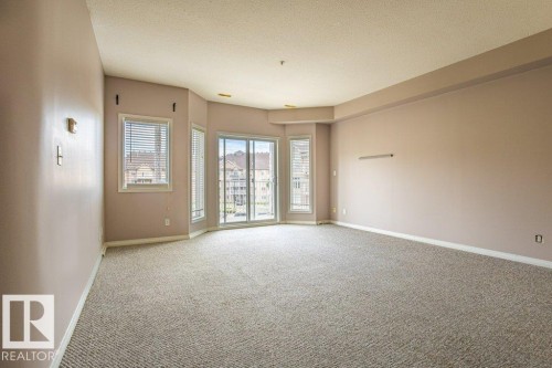 Spacious living area featuring neutral-toned carpet and walls, along with a large sliding glass door and windows providing natural light - 326 4304 139 Ave, Edmonton, AB - Indoor Photo Showing Other Room