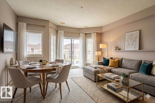 Open-concept living and dining area with a sliding glass door leading to a balcony, featuring a ceiling-mounted television and window blinds - 326 4304 139 Ave, Edmonton, AB - Indoor Photo Showing Living Room