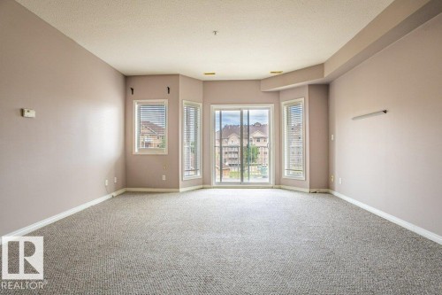 The room features neutral-toned walls, light-colored carpeting, and a bay window with blinds - 326 4304 139 Ave, Edmonton, AB - Indoor Photo Showing Other Room