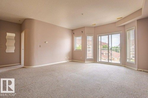 The property features light-colored carpeting, a sliding glass door, and windows with blinds that provide views of the surrounding neighborhood - 326 4304 139 Ave, Edmonton, AB - Indoor Photo Showing Other Room