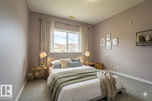 Bedroom featuring a large window with privacy curtains, a tufted headboard, and soft carpet flooring - 326 4304 139 Ave, Edmonton, AB - Indoor Photo Showing Bedroom