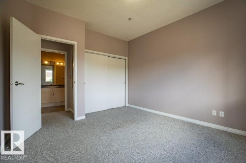 This room features light-colored carpeting, a closet with sliding doors, and a doorway leading to a bathroom with a vanity and mirror - 326 4304 139 Ave, Edmonton, AB - Indoor Photo Showing Other Room