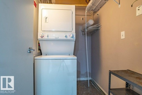 Laundry area featuring a stacked washer and dryer, tile flooring, and wall-mounted shelving - 326 4304 139 Ave, Edmonton, AB - Indoor Photo Showing Laundry Room