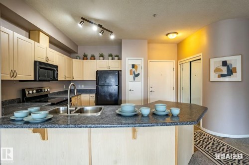 The kitchen features light-toned cabinetry, dark countertops, a double basin sink, and black appliances including a refrigerator, oven, and microwave - 326 4304 139 Ave, Edmonton, AB - Indoor Photo Showing Kitchen With Double Sink