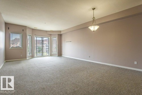 Spacious room featuring carpeting, a light fixture, and a balcony with sliding glass doors and side windows - 326 4304 139 Ave, Edmonton, AB - Indoor Photo Showing Other Room