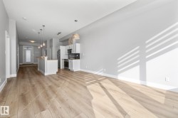 Open concept living space featuring light wood flooring, an eat-in kitchen island, and stainless steel appliances - 