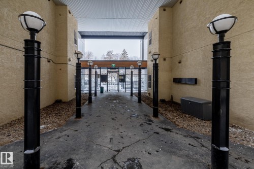 The property features a gated entrance with black lampposts, a concrete pathway, and textured beige exterior walls - 114 10531 117 Street, Edmonton, AB -  With Exterior
