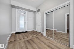 Inviting entryway featuring light-colored hardwood flooring, a white front door with a translucent glass panel, and a mirrored closet with sliding doors - 