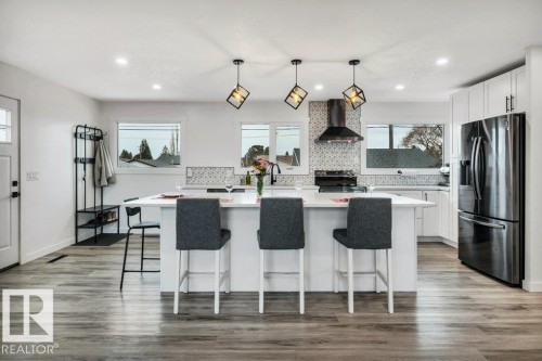 Well-appointed kitchen featuring a large island with seating, a stainless steel refrigerator, and modern pendant lighting fixtures - 6719 94B Avenue, Edmonton, AB - Indoor Photo Showing Kitchen With Upgraded Kitchen