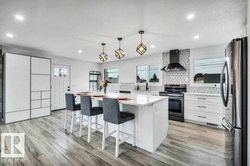The kitchen features a central island with seating for three, sleek white cabinetry, and stainless steel appliances - 6719 94B Avenue, Edmonton, AB - Indoor Photo Showing Kitchen With Upgraded Kitchen