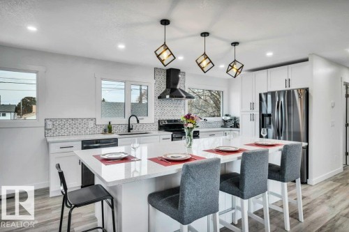 The kitchen features white cabinetry, a large island with seating, stainless steel appliances, and stylish pendant lighting - 6719 94B Avenue, Edmonton, AB - Indoor