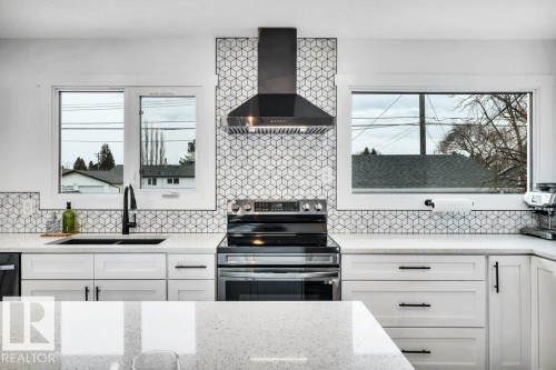 The kitchen features white cabinetry, a black range hood, and a geometric pattern tile backsplash - 6719 94B Avenue, Edmonton, AB - Indoor Photo Showing Kitchen With Double Sink With Upgraded Kitchen