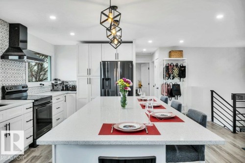 This kitchen features white cabinetry, a large kitchen island with seating, dark appliances, and recessed lighting - 6719 94B Avenue, Edmonton, AB - Indoor