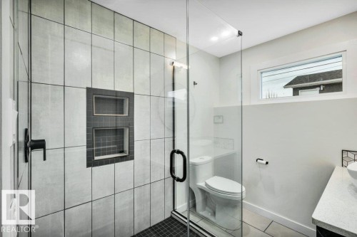 Modern bathroom featuring a glass-enclosed shower with light-colored wall tiles and dark-colored recessed shelves, a toilet, and a vanity with a light-colored countertop - 6719 94B Avenue, Edmonton, AB - Indoor Photo Showing Bathroom
