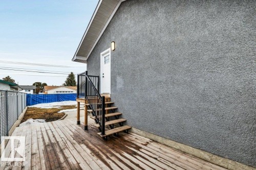 The property features a stucco exterior, a wooden deck, and exterior stairs with a black metal railing leading to a white exterior door - 6719 94B Avenue, Edmonton, AB - Outdoor