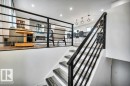 Staircase featuring dark wood treads and a contemporary black metal railing, leading to a living area with a fireplace and views of a kitchen island with pendant lighting - 6719 94B Avenue, Edmonton, AB  - Indoor Photo Showing Other Room 
