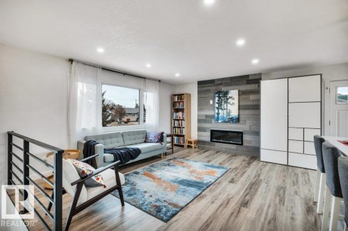 Living area featuring wood-look flooring, a fireplace with a textured wall, and recessed lighting - 6719 94B Avenue, Edmonton, AB - Indoor Photo Showing Living Room With Fireplace