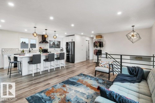 This open-concept living area features light wood-style flooring, a spacious kitchen island with seating, pendant lighting, and recessed ceiling lights - 6719 94B Avenue, Edmonton, AB - Indoor Photo Showing Other Room