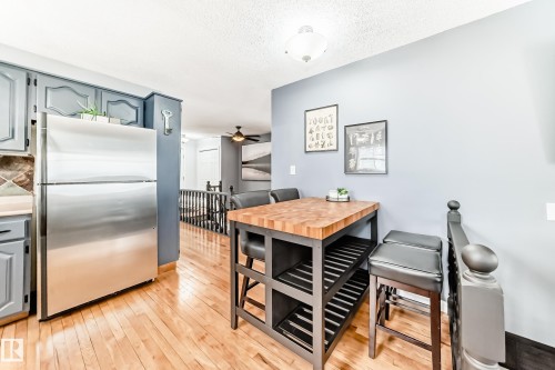 Kitchen and dining area featuring hardwood floors, a stainless steel refrigerator, and blue cabinetry - 17819 91A Street, Edmonton, AB - Indoor