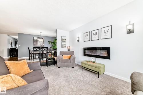 The living area features a wall-mounted electric fireplace, wall sconces, and carpeted flooring - 17819 91A Street, Edmonton, AB - Indoor Photo Showing Living Room With Fireplace