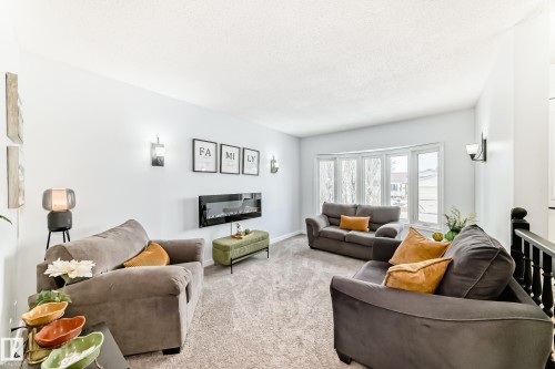 The living area features a carpeted floor, a bay window, and a wall-mounted electric fireplace - 17819 91A Street, Edmonton, AB - Indoor Photo Showing Living Room With Fireplace