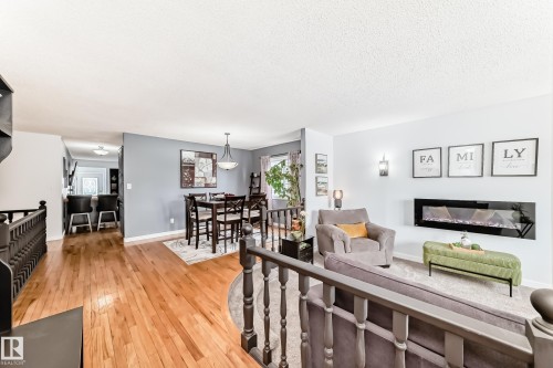 The interior features hardwood flooring, a dining area with a chandelier, and a living area with a wall-mounted fireplace - 17819 91A Street, Edmonton, AB - Indoor Photo Showing Living Room With Fireplace