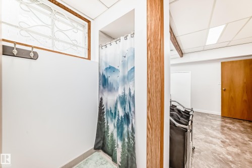 The property features a shower area with a decorative curtain, a window with a security griller, and a coat rack on the wall - 17819 91A Street, Edmonton, AB - Indoor Photo Showing Other Room