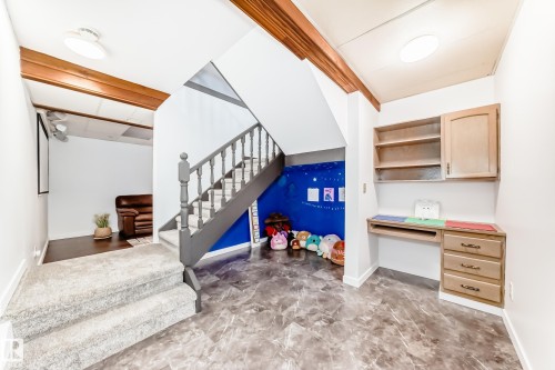 This versatile space features a staircase with carpeted treads and a painted railing, exposed wooden beams on the ceiling, and a built-in desk with shelving - 17819 91A Street, Edmonton, AB - Indoor Photo Showing Other Room