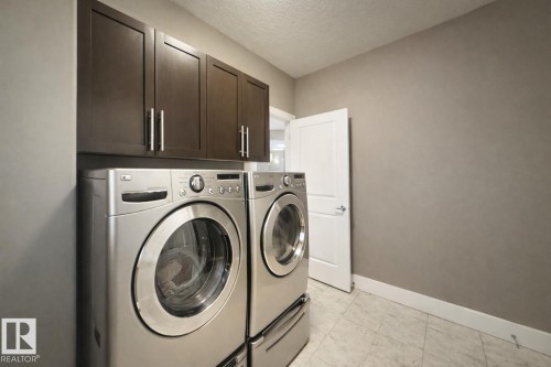 The laundry area features dark wood cabinetry with silver hardware, a tiled floor, and a white door - 6712 18 Ave Sw Sw, Edmonton, AB - Indoor Photo Showing Laundry Room