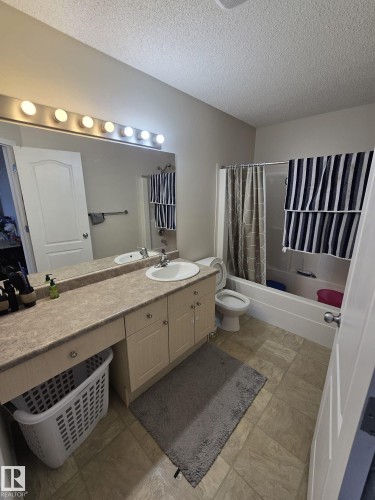 The bathroom features a vanity with an integrated sink, a large mirror with overhead lighting, a toilet, and a shower-tub combination - 3311 21 Street, Edmonton, AB - Indoor Photo Showing Bathroom