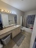 The bathroom features a vanity with an integrated sink, a large mirror with overhead lighting, a toilet, and a shower-tub combination - 3311 21 Street, Edmonton, AB  - Indoor Photo Showing Bathroom 