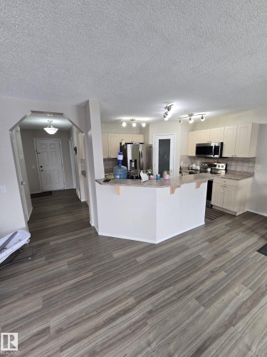 Open concept kitchen featuring light-colored cabinetry, stainless steel appliances, and a central island with a breakfast bar - 3311 21 Street, Edmonton, AB - Indoor Photo Showing Kitchen