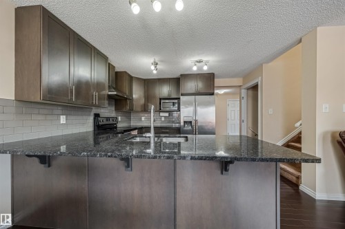 The kitchen features a large island with a dark granite countertop and a stainless steel sink, dark wood cabinetry, and a grey subway tile backsplash - 2314 22 Avenue, Edmonton, AB - Indoor Photo Showing Kitchen With Upgraded Kitchen