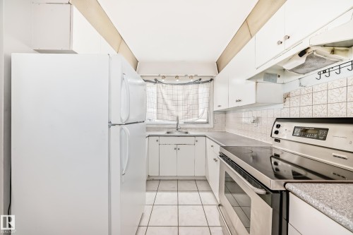 The kitchen features a white refrigerator, white cabinetry, and stainless steel appliances including a range and an overhead exhaust fan - 12411 126 Street Nw, Edmonton, AB - Indoor Photo Showing Kitchen