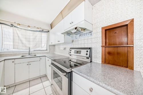 The kitchen features white cabinetry, a stainless steel range, a double basin sink, and tile flooring - 12411 126 Street Nw, Edmonton, AB - Indoor Photo Showing Kitchen