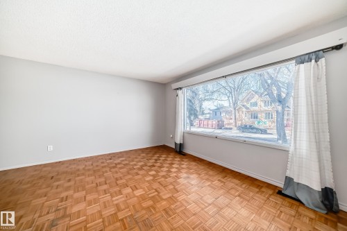 This room features parquet flooring and a large picture window, which provides views of the street and surrounding properties - 12411 126 Street Nw, Edmonton, AB - Indoor Photo Showing Other Room