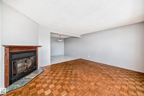 Living area featuring wood parquet flooring, a fireplace with a wood mantle and marble hearth, and light gray walls - 12411 126 Street Nw, Edmonton, AB - Indoor With Fireplace