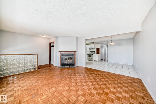 The property features distinctive parquet flooring in the main living area, complemented by a corner fireplace with a wooden mantel - 12411 126 Street Nw, Edmonton, AB - Indoor Photo Showing Other Room With Fireplace
