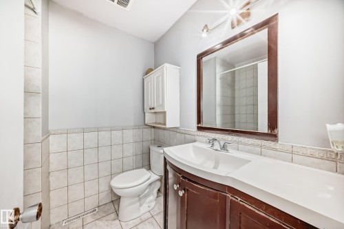 Bathroom featuring a vanity with a white countertop and dark wood cabinetry, a mirror with a wood frame, and white wall tiles - 12411 126 Street Nw, Edmonton, AB - Indoor Photo Showing Bathroom