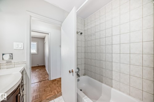The bathroom features a tiled shower with a bathtub, a white vanity countertop, and light-colored wall tiles - 12411 126 Street Nw, Edmonton, AB - Indoor Photo Showing Bathroom