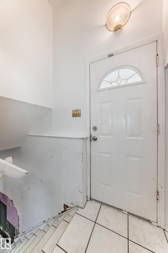 Entryway with a white paneled door featuring an arched window with decorative glass, overhead lighting, and white tiled flooring - 12411 126 Street Nw, Edmonton, AB - Indoor Photo Showing Other Room