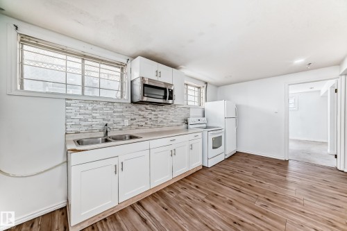 The kitchen features white cabinetry, a tiled backsplash, and wood-style flooring - 12411 126 Street Nw, Edmonton, AB - Indoor Photo Showing Kitchen With Double Sink