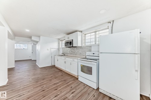 The property features a kitchen with white cabinetry, a stainless steel microwave, a white electric range, and a white refrigerator - 12411 126 Street Nw, Edmonton, AB - Indoor Photo Showing Kitchen