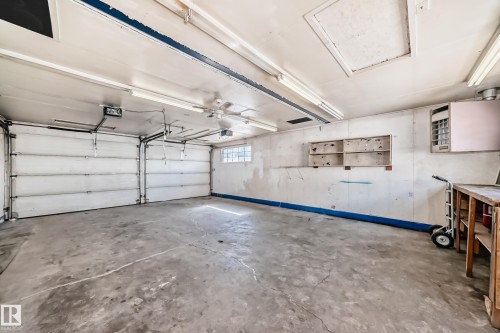 The property features a garage with two overhead doors, a concrete floor, and fluorescent lighting fixtures - 12411 126 Street Nw, Edmonton, AB - Indoor Photo Showing Garage